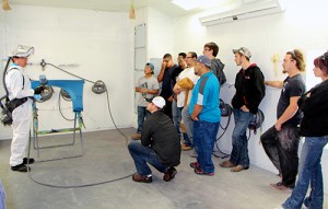 A photo of event attendees listening to the waterborne spray paint demonstration inside Dunwoody's spray paint booth 