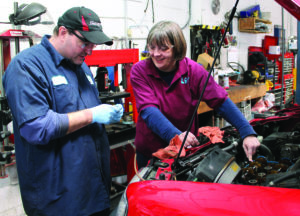 Cathy Heying and a staff member of The Life Garage work on repairing a red car. 