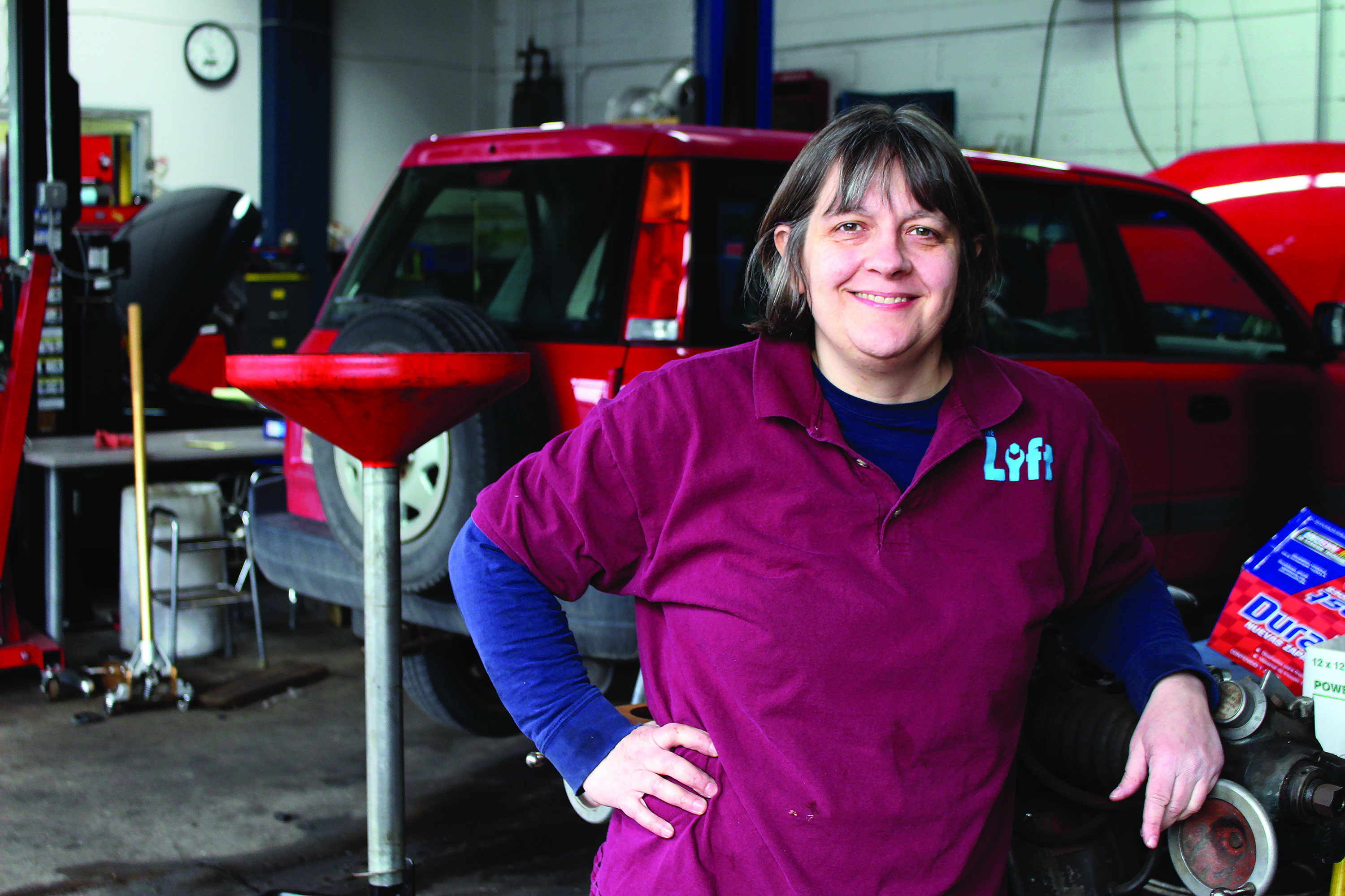 Cathy Heying, Dunwoody Alumni and founder of The Lift Garage, stands next to a car she is repairing. Headshot.