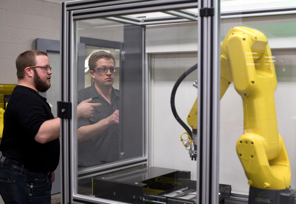 Two students looking at the robotic arm that's part of the Fanuc MTEC