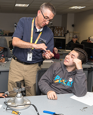 E.J. Daigle, left, Dean of Robotics & Manufacturing, answers a question Mark Velez had about connecting wires while building a flashlight in a lab.