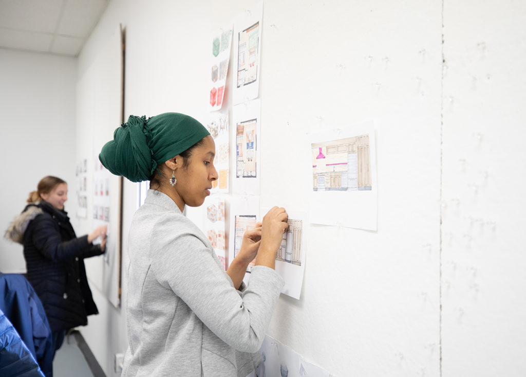 Interior Design student Sumeya Mohamed pins her work to the board during class.