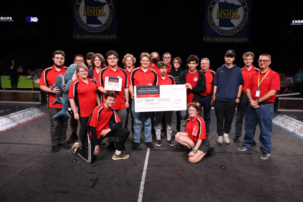 The Roseville FIRST Robotics team posing with their mentors, a giant check (meant to symbolize their $500 award from Dunwoody), and Dean E.J. Daigle