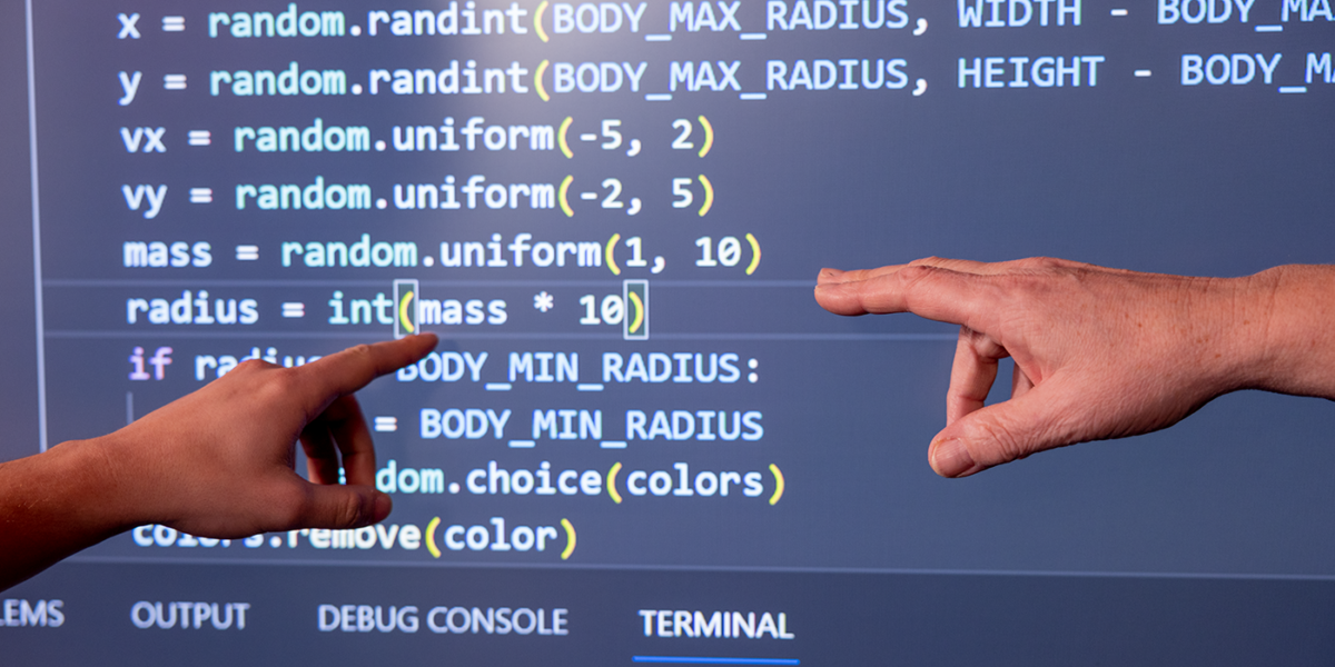 Image of hands pointing to a screen with code.