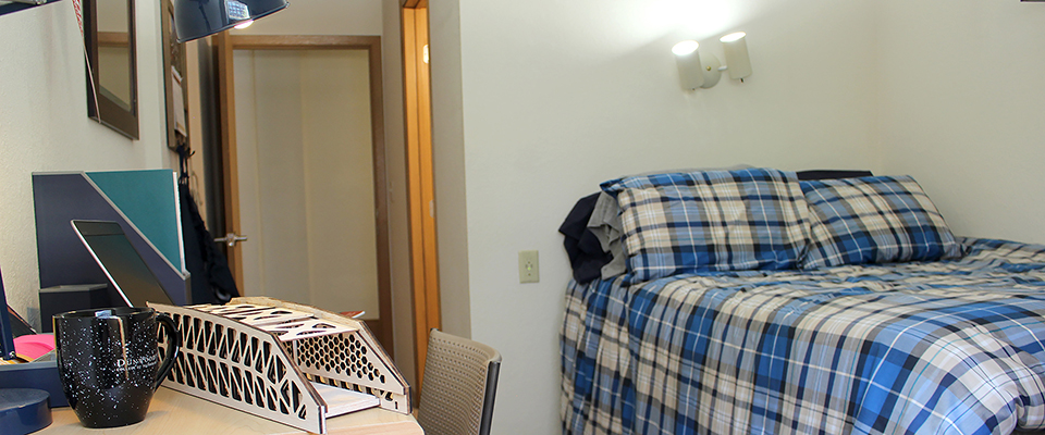 A twin bed next to a desk with chair and lamp