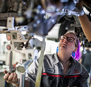 Photo of a women Automotive student working on a vehicle in the Auto lab
