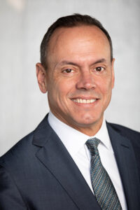 Headshot of Alfredo Martel wearing a charcoal suit with a gray striped tie