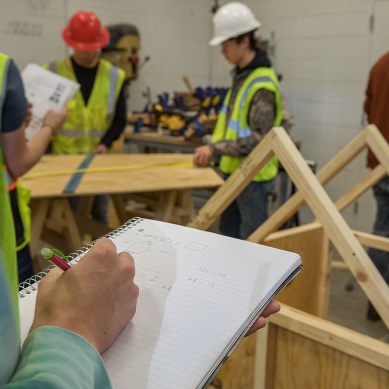 Students wearing hard hats and high viz vests while looking at construction plans in one of Dunwoody's facilities management courses