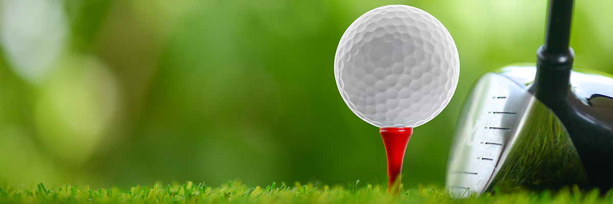 Photo of a golf ball on a tee set into green grass with a golf club next to it
