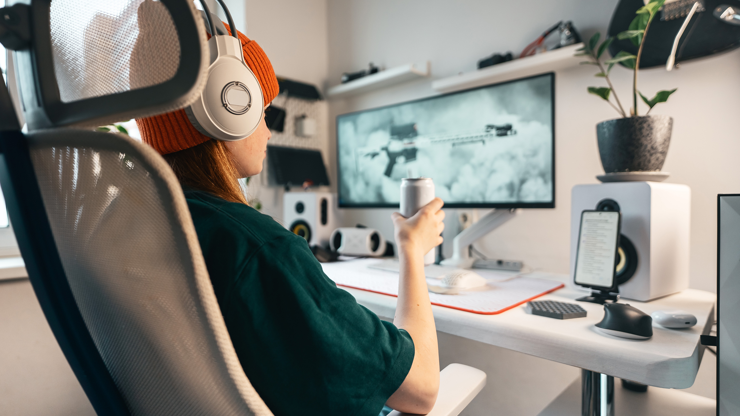 A gamer wearing headphones and sitting in a chair with a large monitor