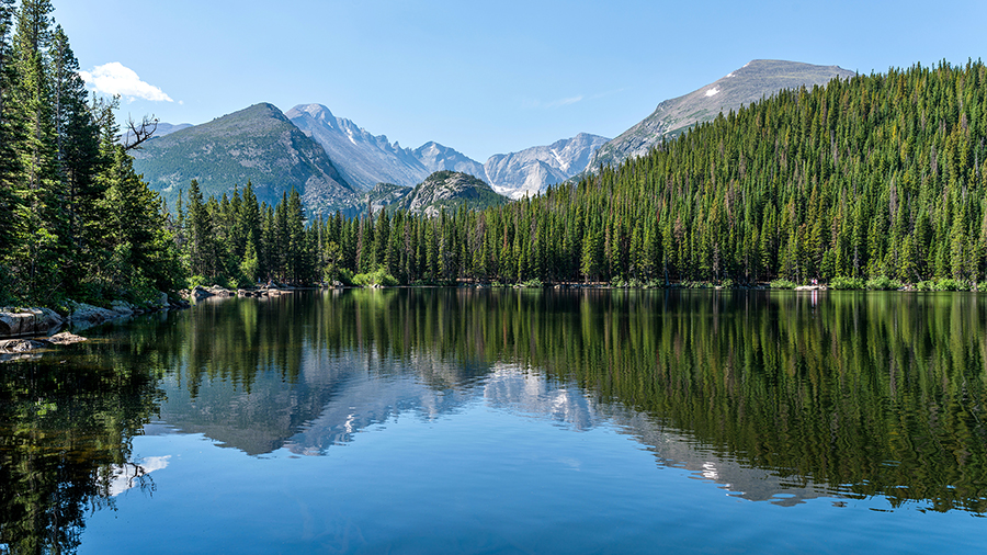 Photo of a lake surrounded by trees with mountains in the background